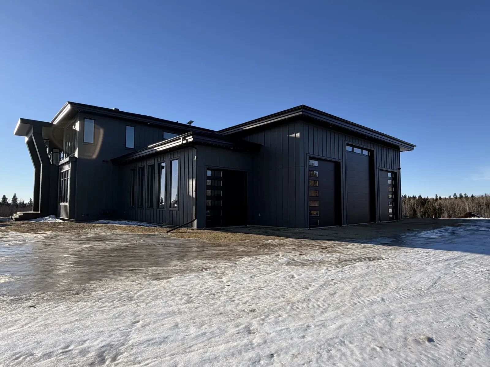 Completed custom acreage home near Lacombe with dark board-and-batten siding, black-framed windows and a triple attached garage, finished by PJM Home Advantage