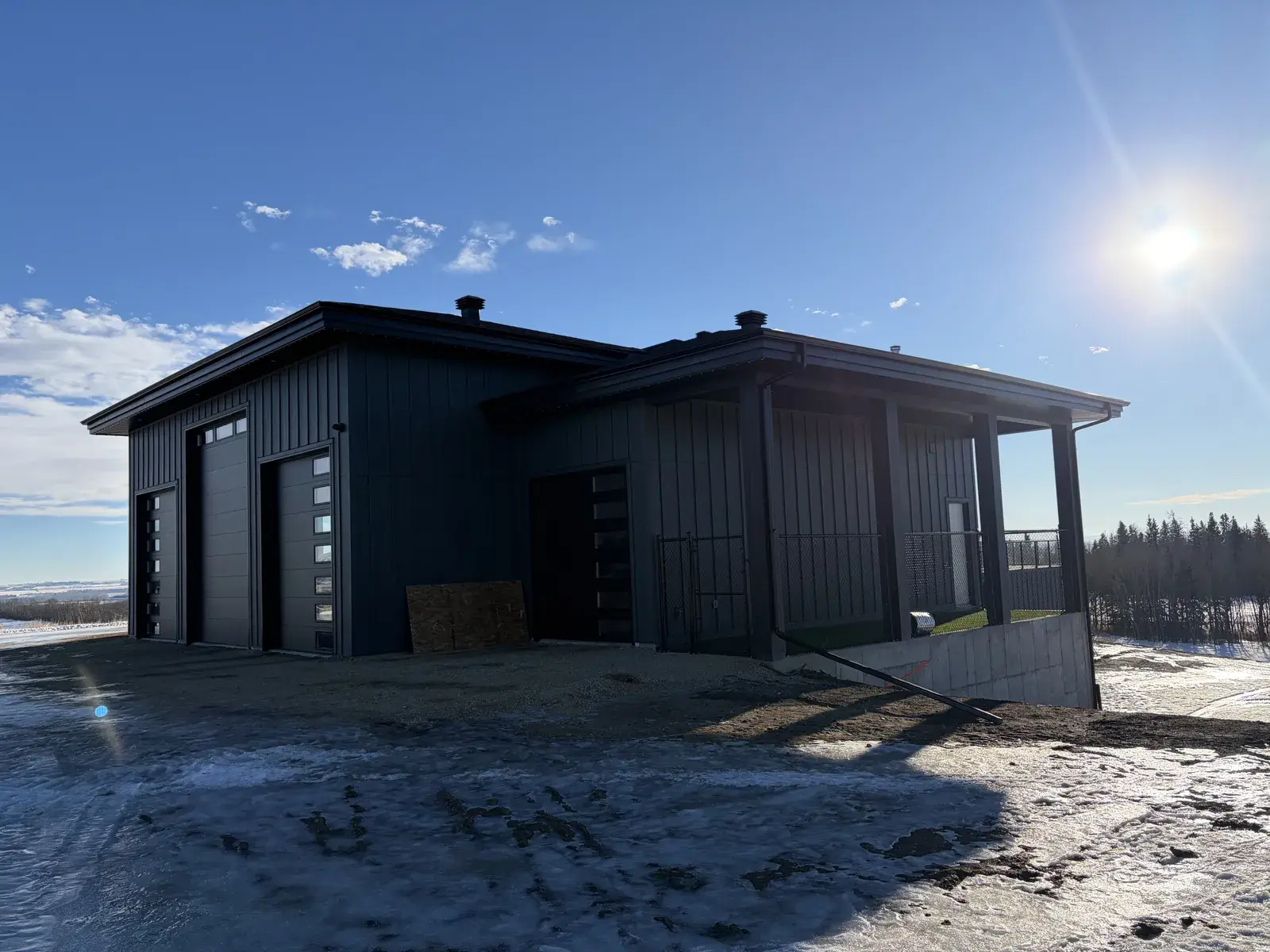 Garage wing of a Lacombe-area acreage home in dark board-and-batten siding with a covered entry, finished soffit and fascia by PJM