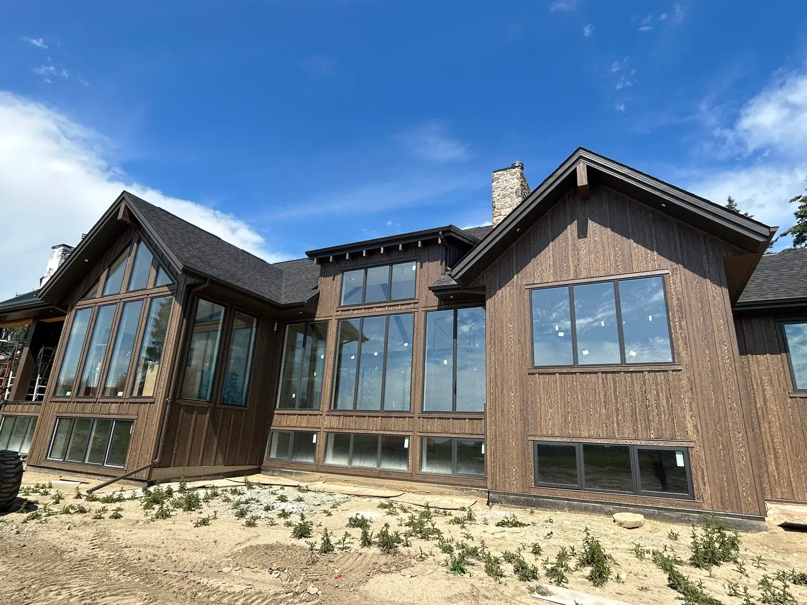 Large acreage home near Red Deer clad in dark-stained vertical wood siding with expansive wraparound glazing under a clear blue sky, finished by PJM