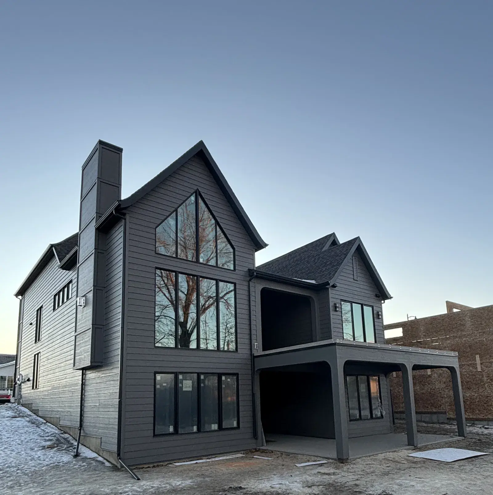 Modern Red Deer-area new build finished in dark board-and-batten and lap siding with black-framed windows and a covered patio, by PJM Home Advantage