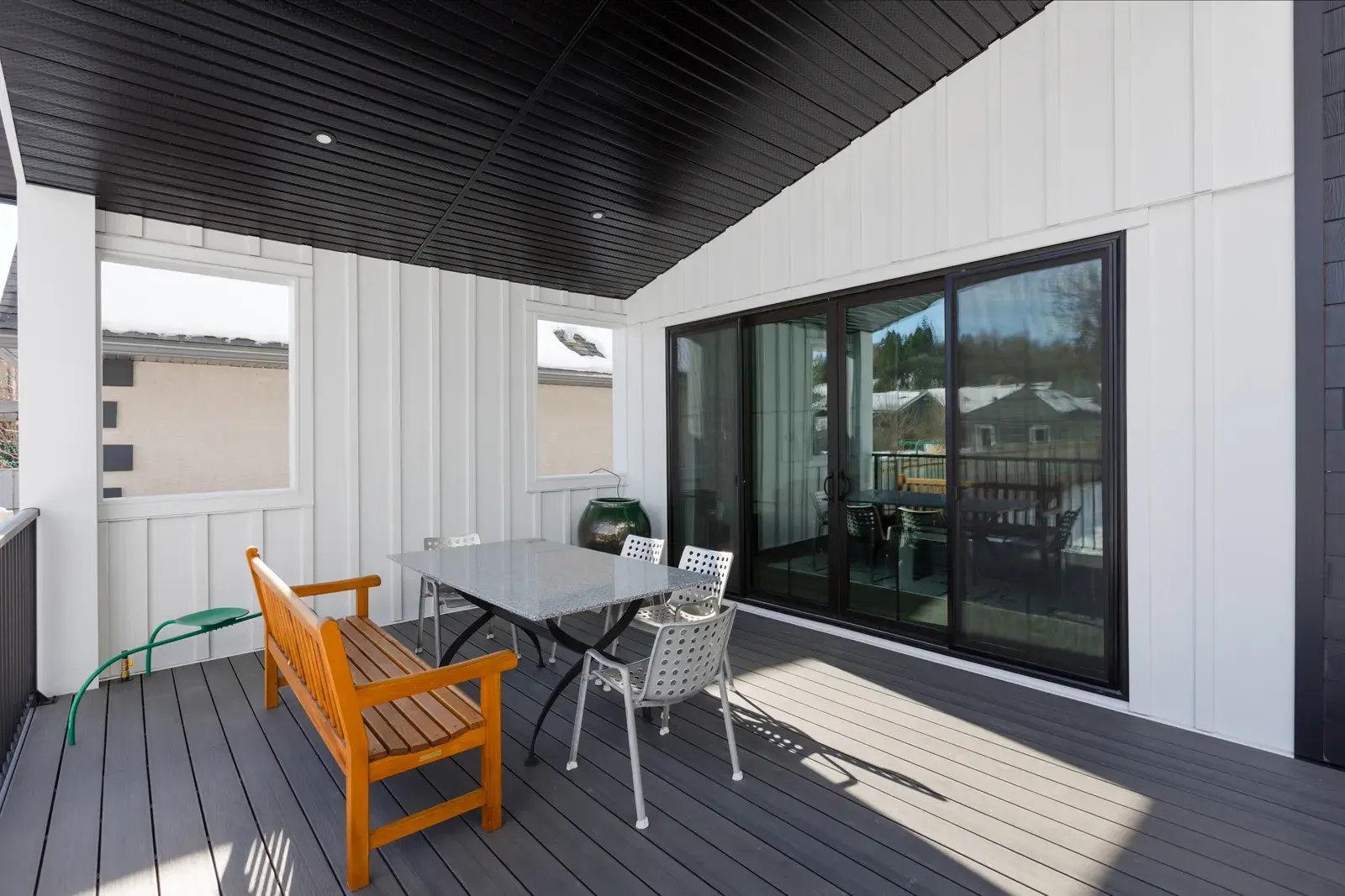 Covered outdoor living deck with white board-and-batten siding, dark soffit and composite decking on a Red Deer home by PJM