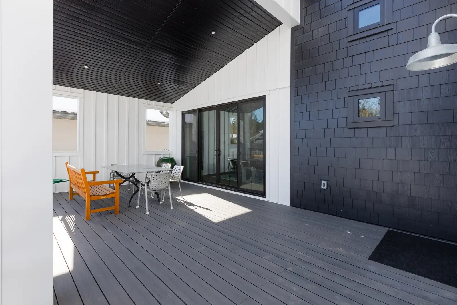 Covered deck on a Red Deer home with a dark navy shake accent wall, white board-and-batten and composite decking, finished by PJM