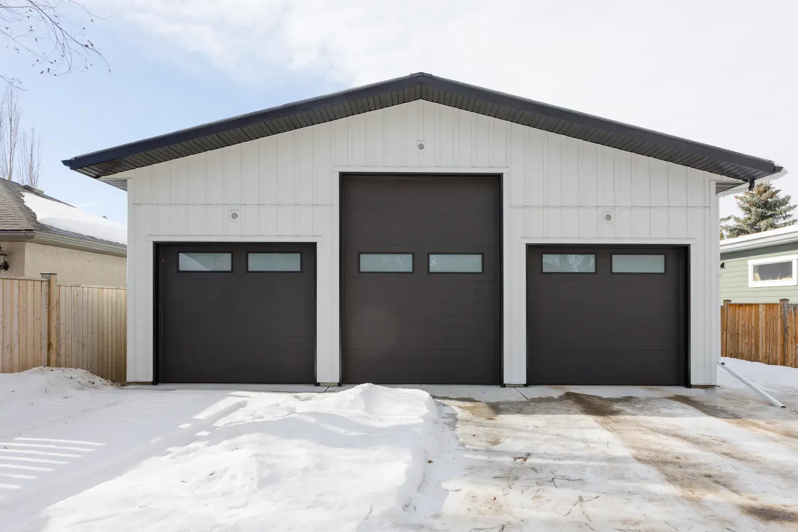 Detached three-bay garage in Red Deer clad in white board-and-batten with dark trim and doors to match the house, by PJM Home Advantage