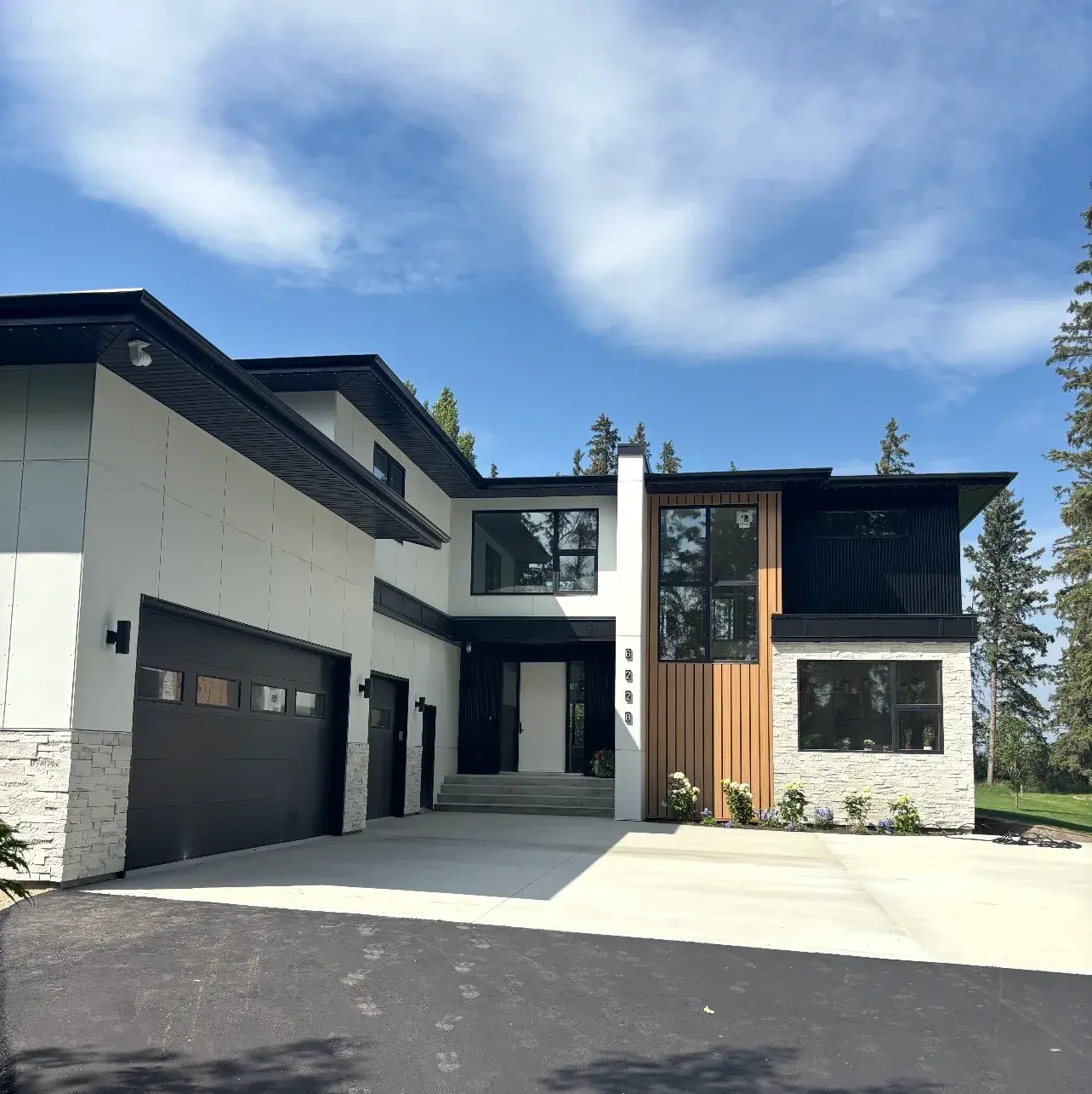 Modern two-storey custom home in Red Deer built by Downton & Co. — white panel and black board-and-batten siding with a vertical wood accent, stone base and black-framed windows, exterior finished by PJM Home Advantage