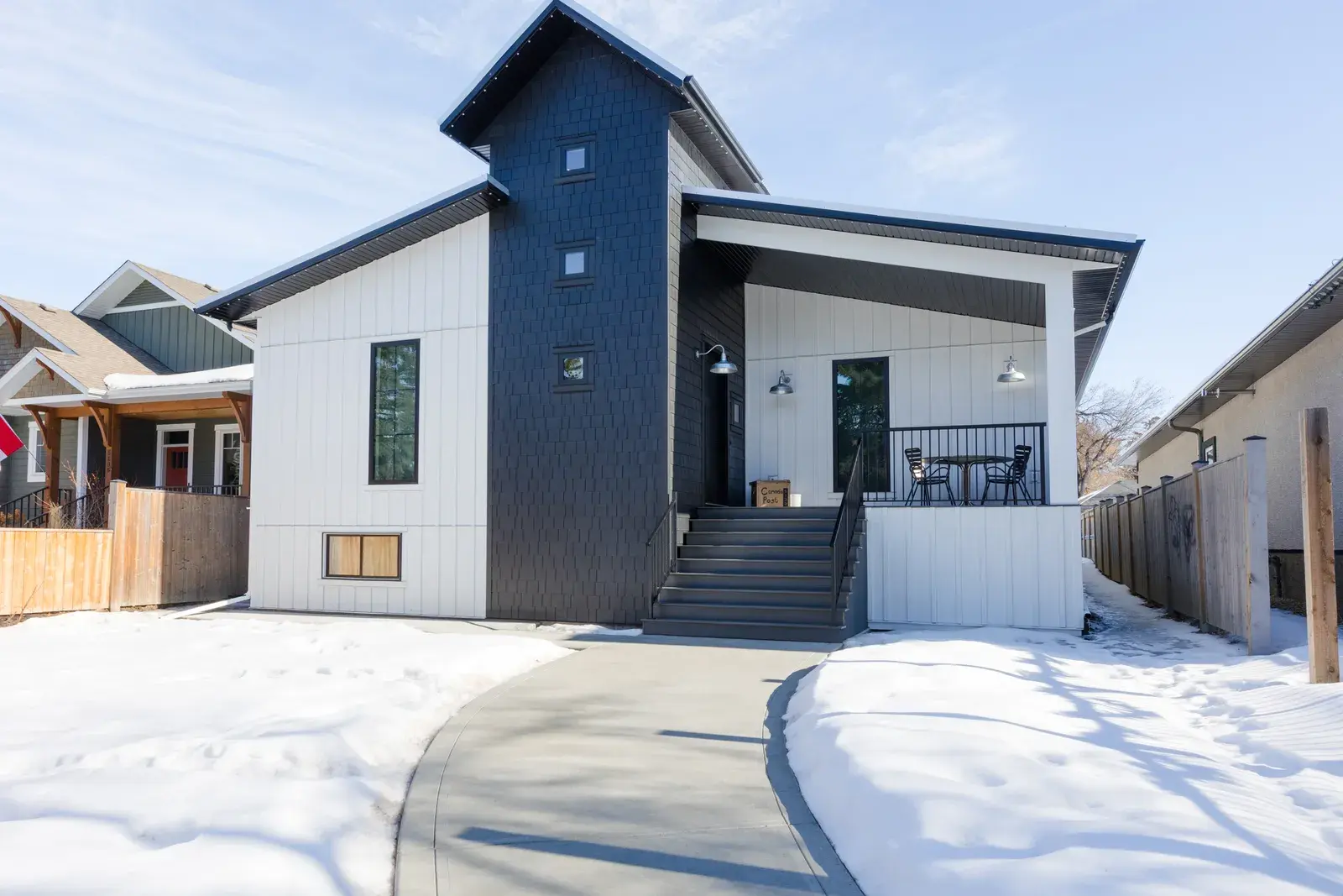 Modern Red Deer home with white board-and-batten siding, a dark navy accent gable and a covered front porch, finished by PJM Home Advantage
