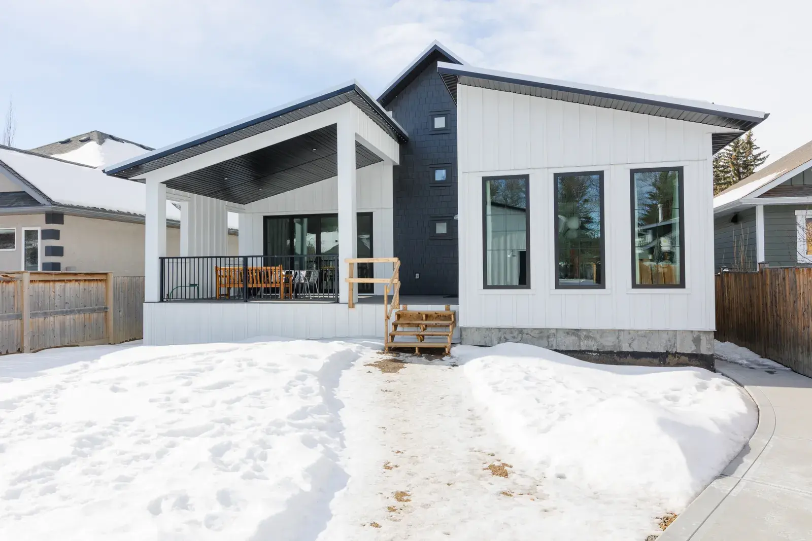 Rear of a Red Deer home in white board-and-batten with a dark navy shake accent and a covered porch, finished by PJM