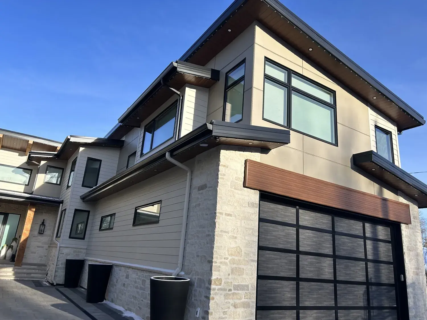 Modern stone-and-wood home in Red Deer with dark seamless eavestrough and 3x4 rectangular downspouts directing water away from the foundation