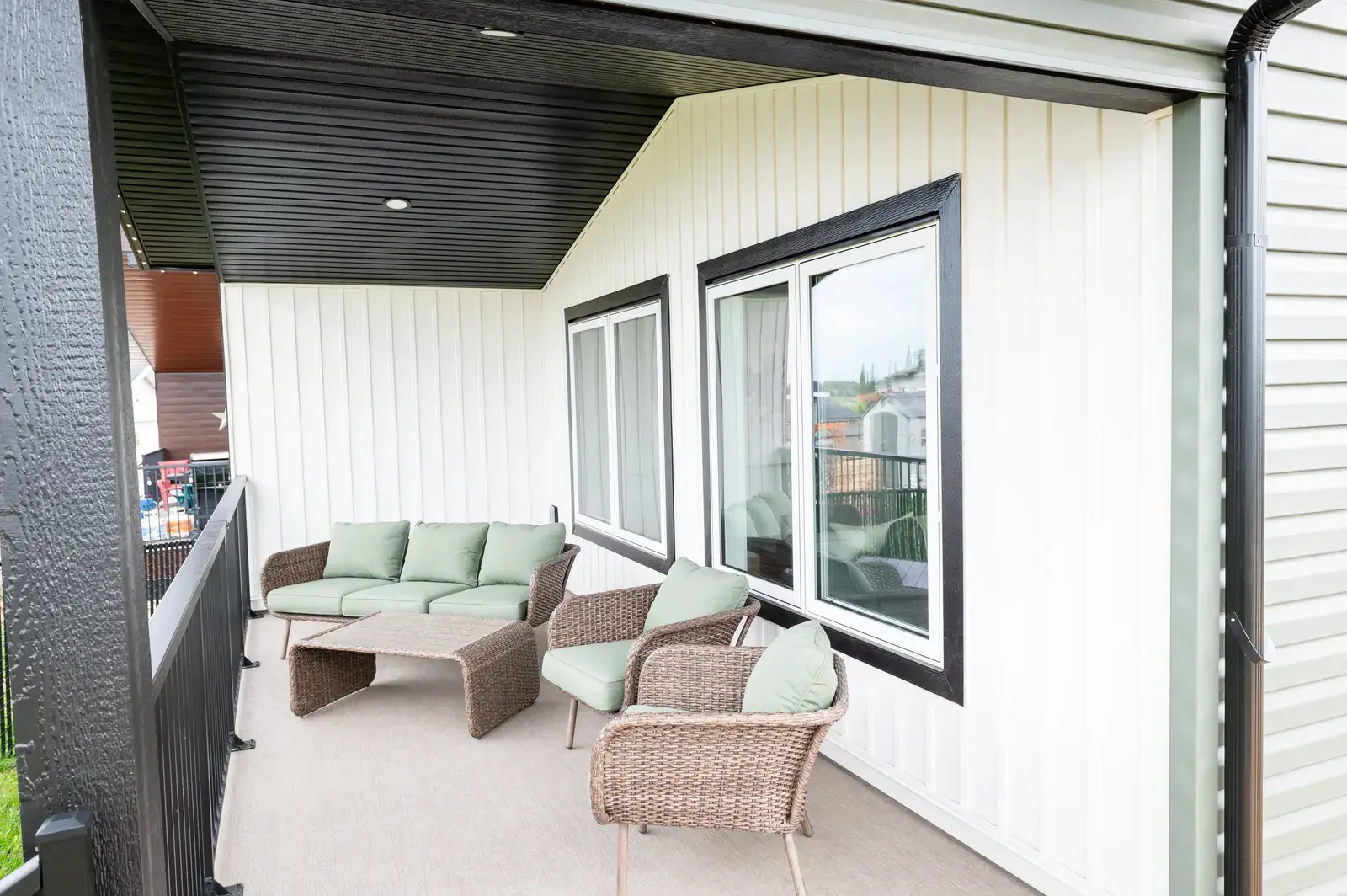 Covered deck with white board-and-batten siding, dark soffit and an outdoor living space on a Blackfalds-area home by PJM