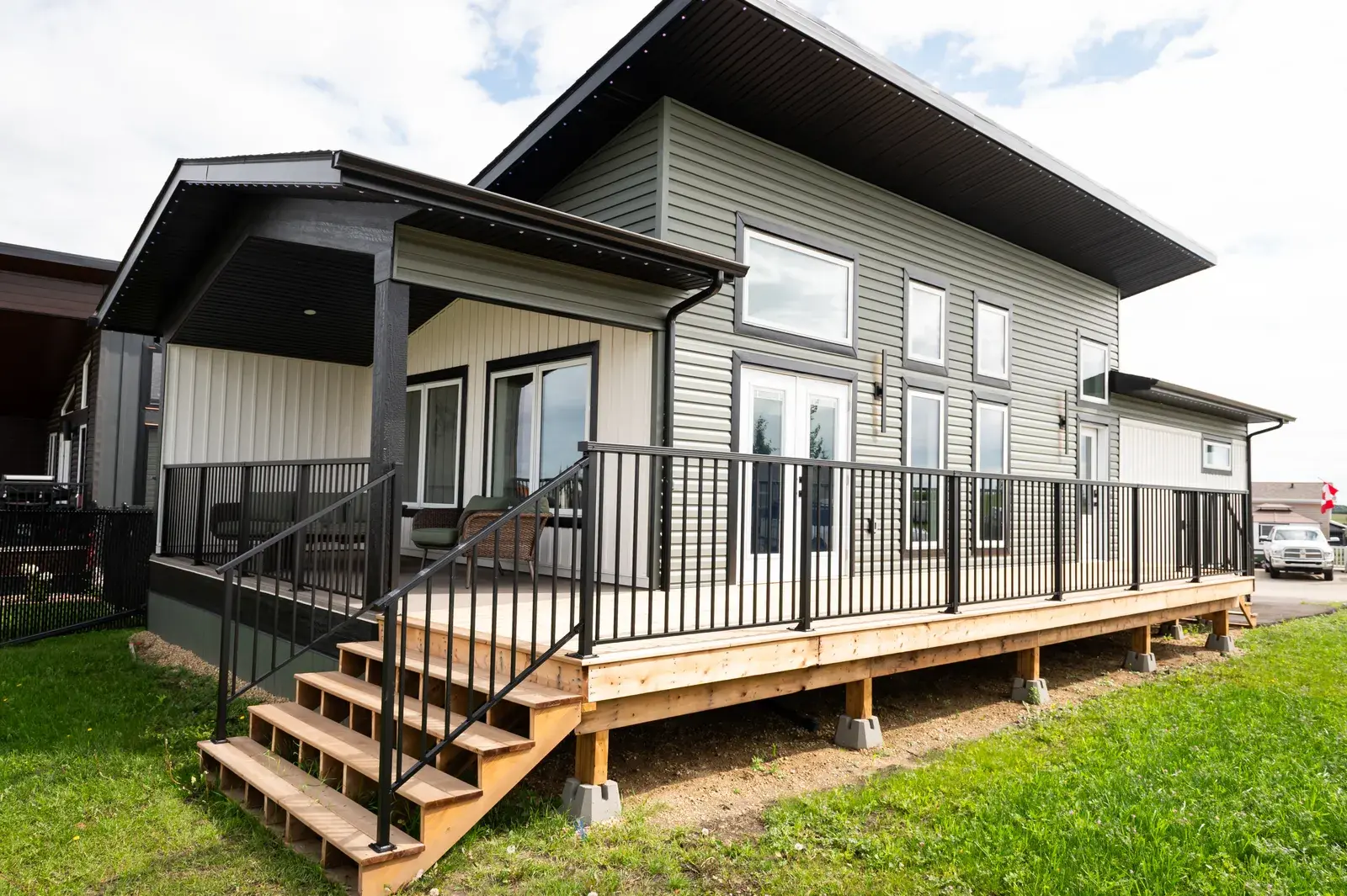 Rear of a Blackfalds-area home in sage-green lap siding with a covered porch, wood deck and black railings, finished by PJM Home Advantage