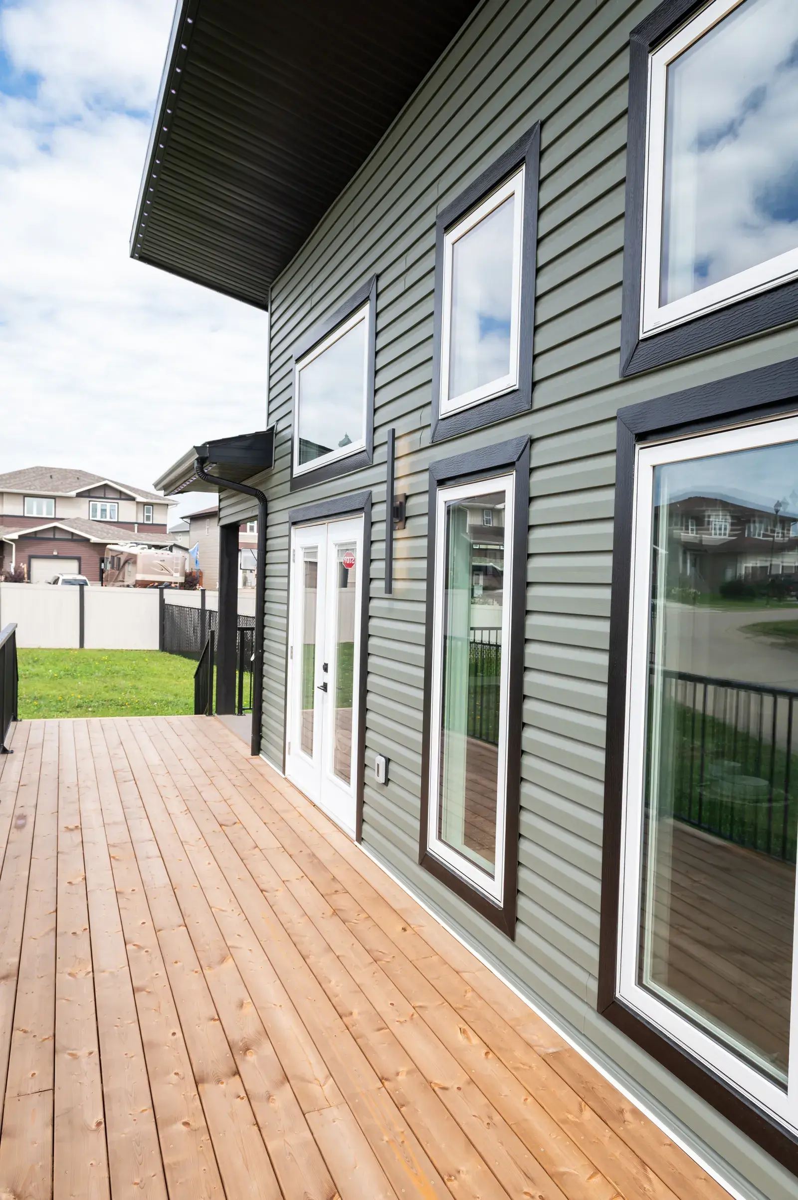 Sage-green lap siding with dark-trimmed windows and a finished wood deck on a Blackfalds-area home by PJM