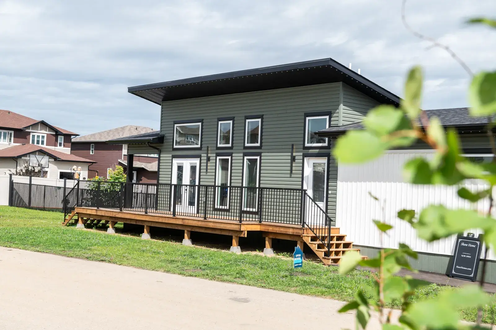 Compact modern build in the Blackfalds area with green lap siding, a dark shed roof and a wood deck, finished by PJM