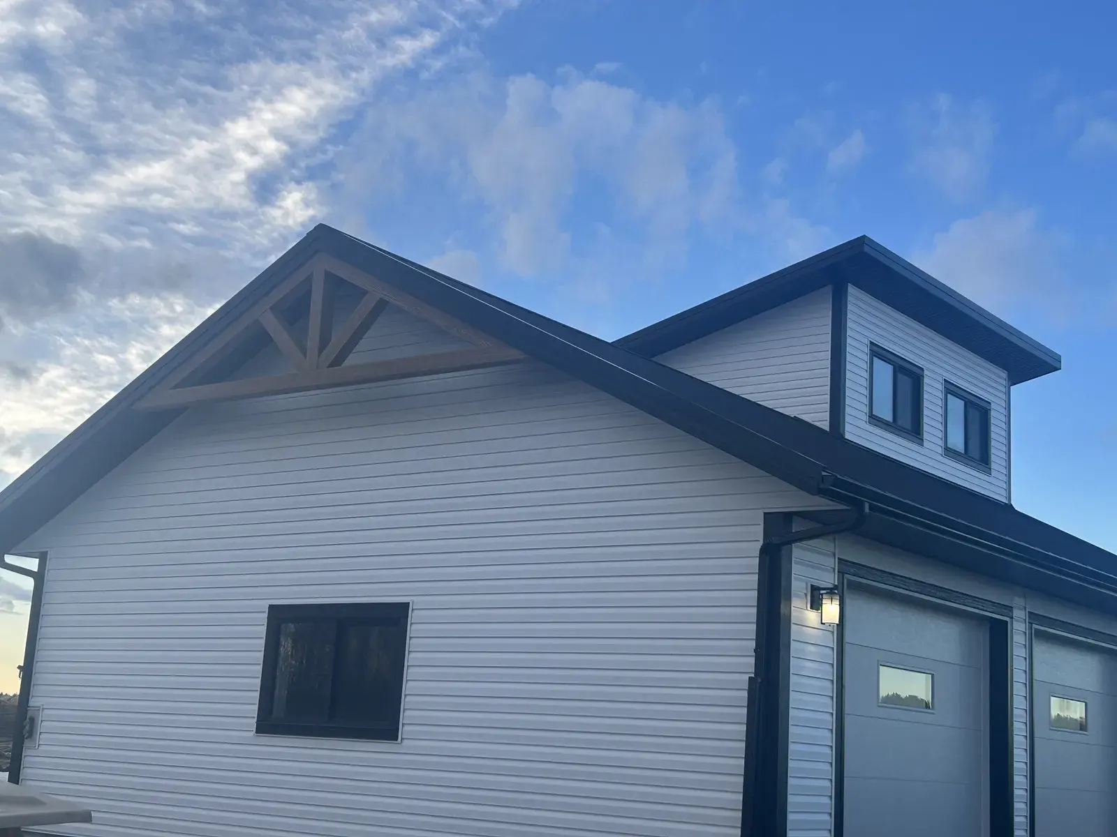 Gable end of a Rimbey-area shop with white lap siding, a steel roof and a timber gable accent at dusk, finished by PJM Home Advantage