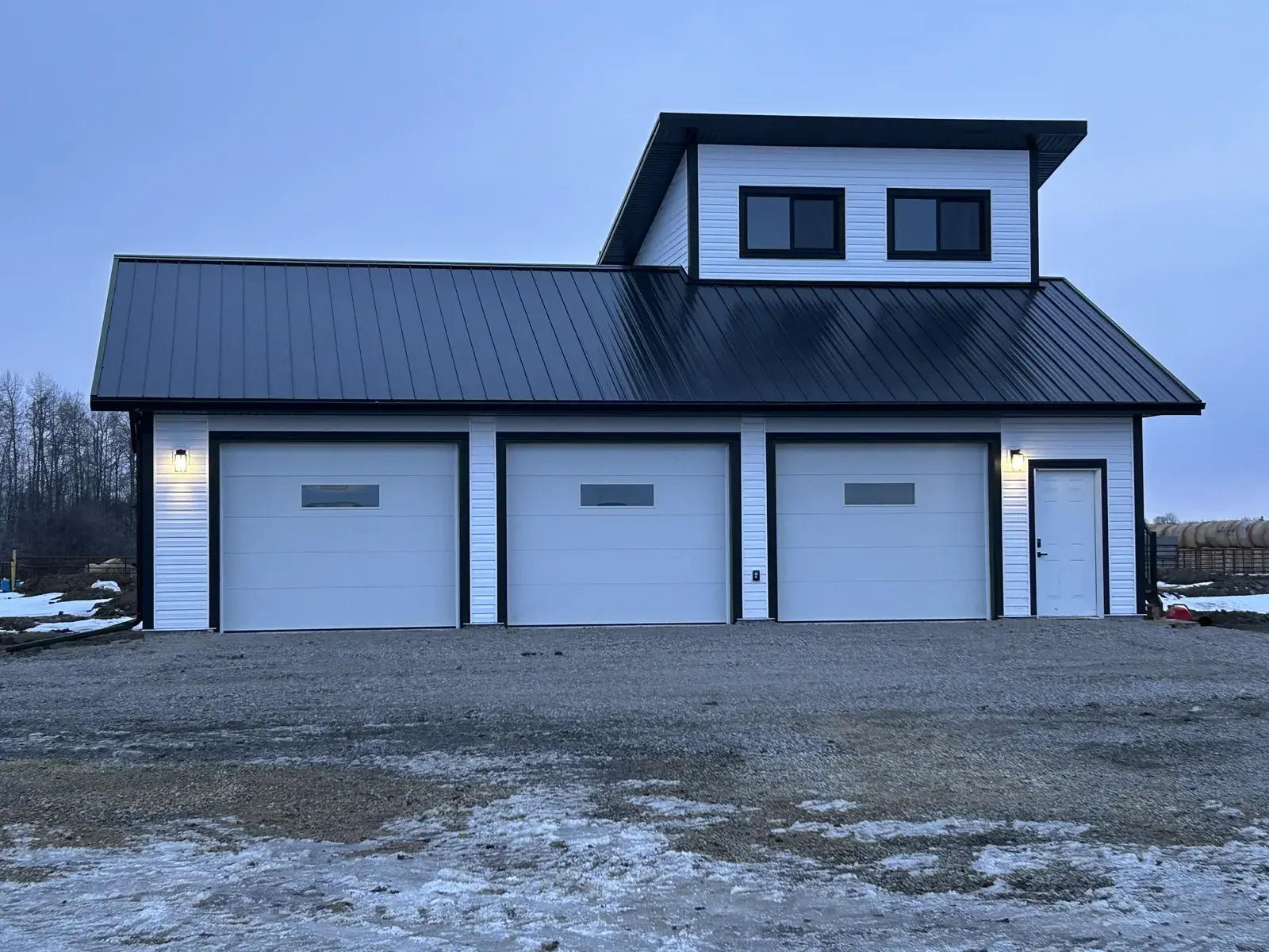 Completed shop and garage near Rimbey with white lap siding, black standing-seam steel roofing and dark trim, finished by PJM Home Advantage