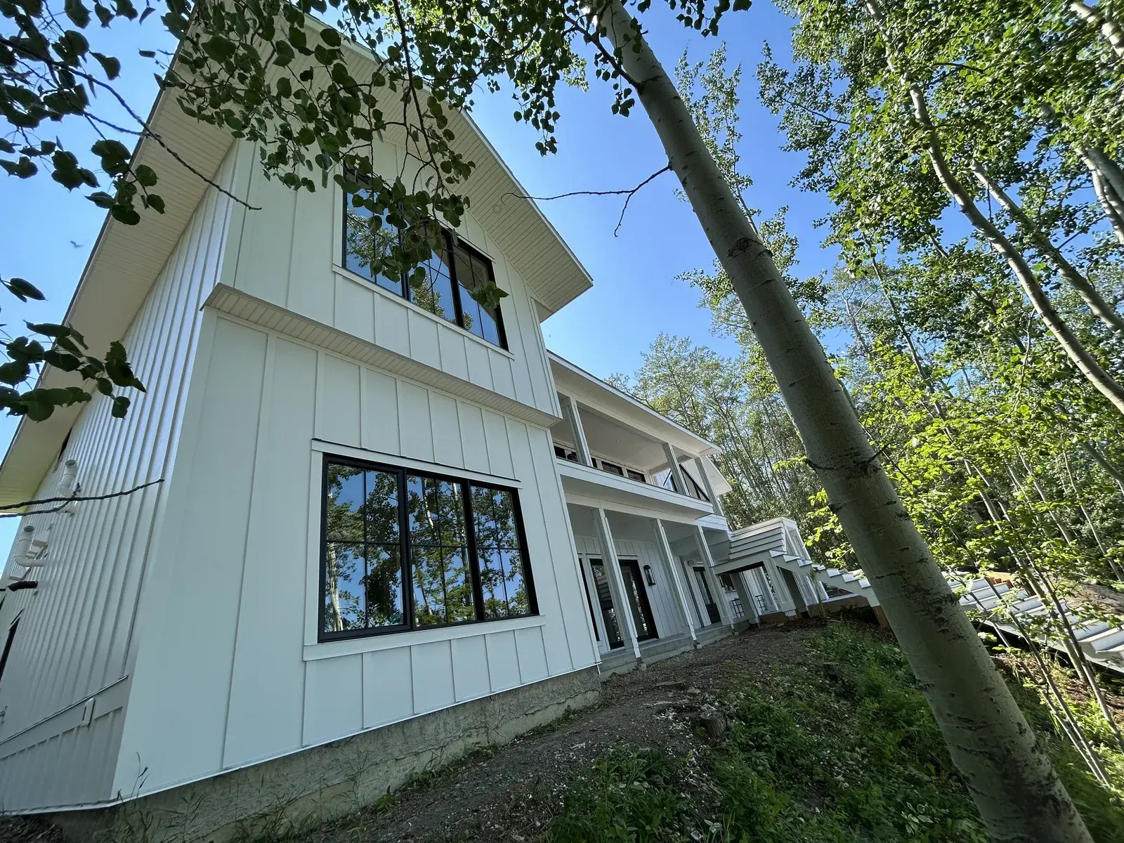 Tall white board-and-batten lake home set among the aspens near Sylvan Lake with large black-framed windows and a covered deck, finished by PJM