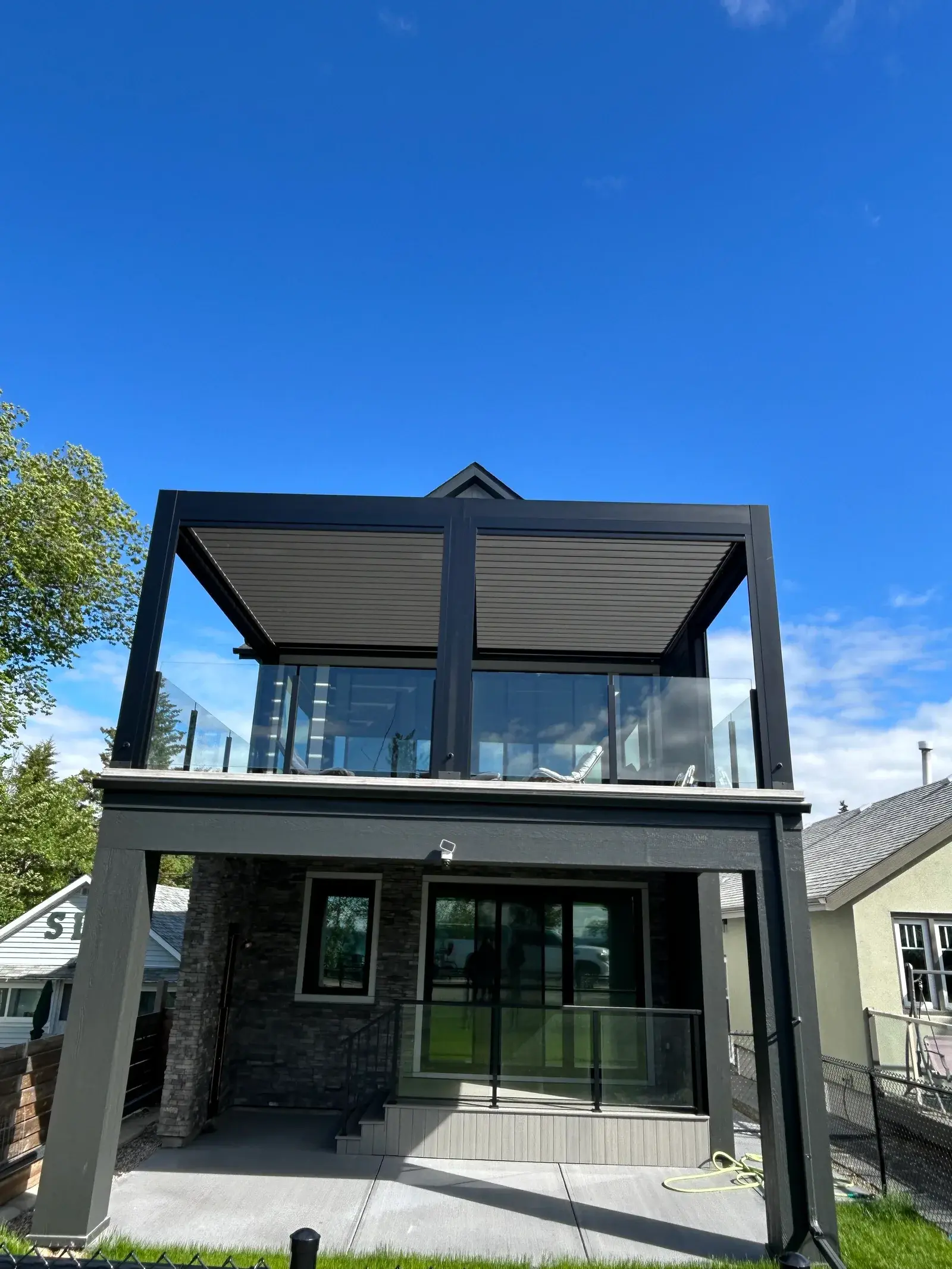 Dark modern home in Sylvan Lake with a glass-railed deck and a motorized louvered pergola over a stone-base lower level, finished by PJM Home Advantage