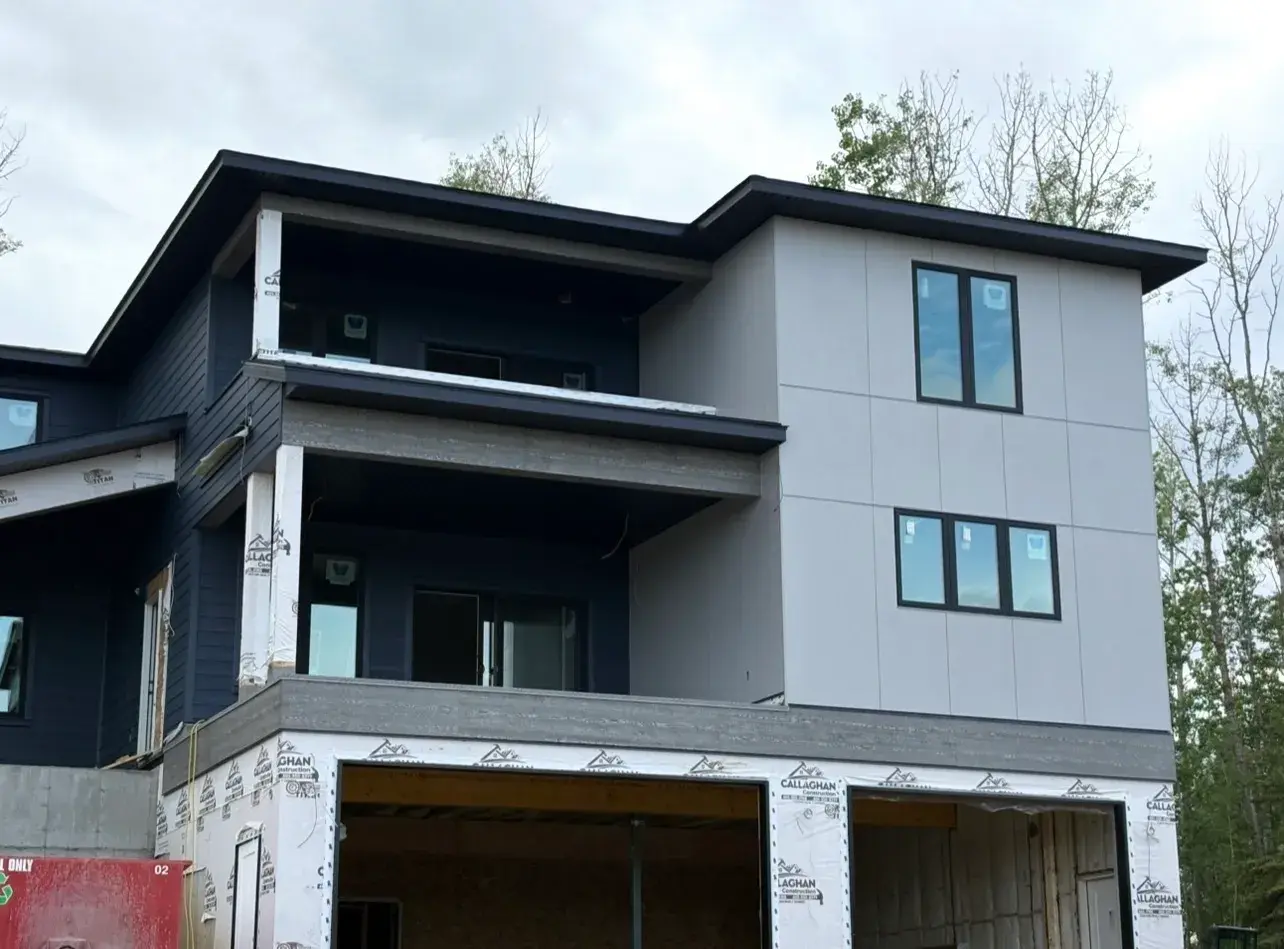 Modern three-storey lake build near Sylvan Lake combining grey panel cladding with dark board-and-batten and covered balconies, exterior by PJM