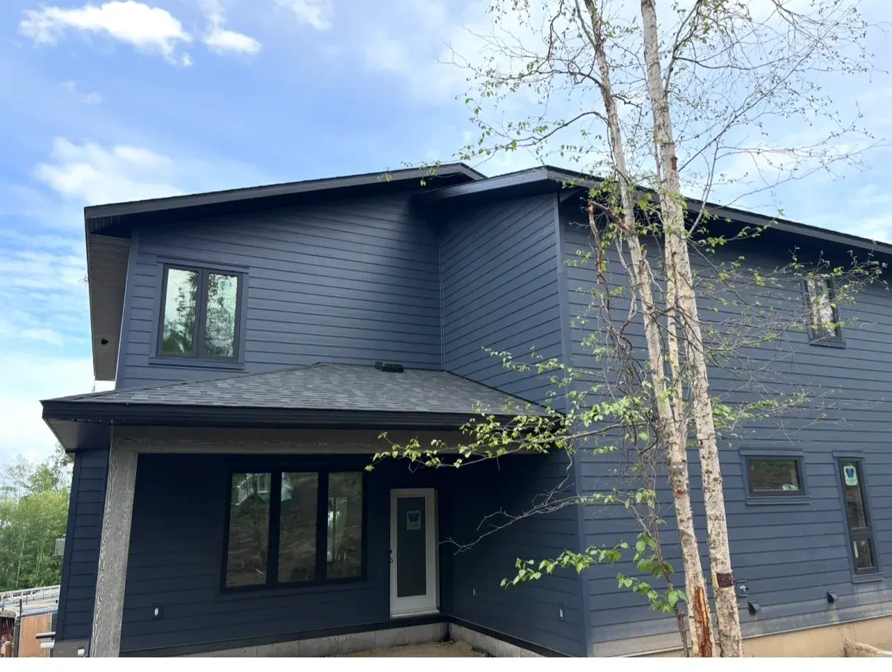 Two-storey home near Sylvan Lake clad in deep navy lap siding with a covered entry and black-framed windows, finished by PJM