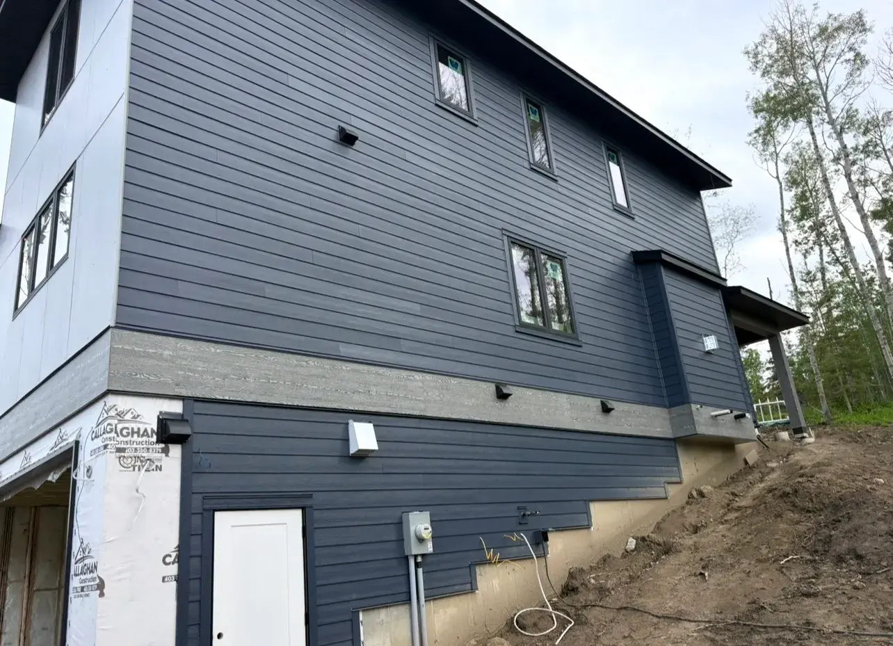 Walk-out side elevation of a Sylvan Lake-area home in deep navy lap siding with finished soffit and fascia by PJM