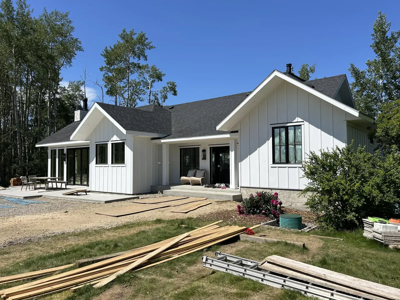 White board-and-batten modern farmhouse near Sylvan Lake with a covered porch and dark shingle roof, siding and trim finished by PJM