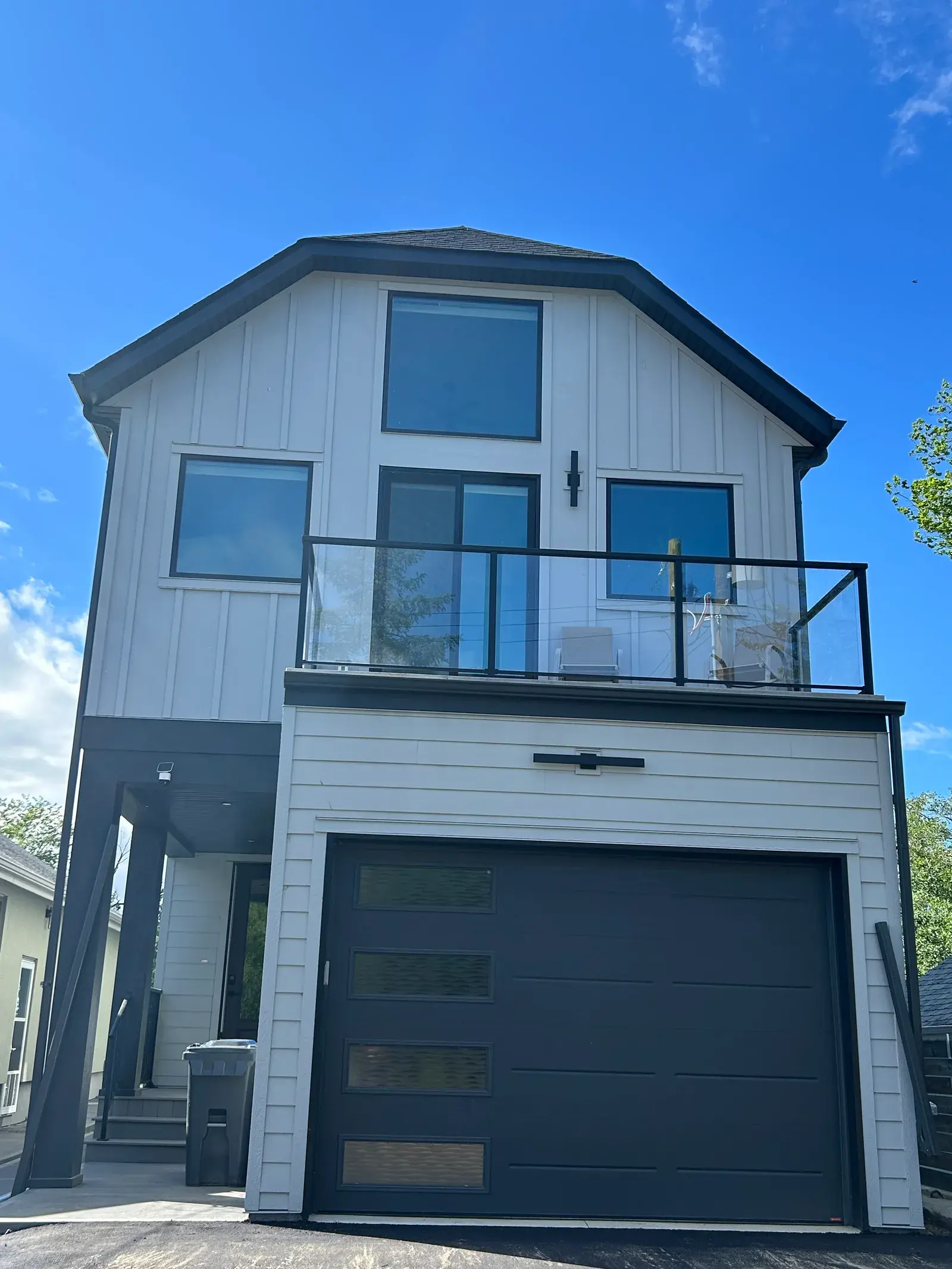 Tall modern home in Sylvan Lake with white board-and-batten and lap siding, a glass-railed balcony and a dark garage, finished by PJM Home Advantage