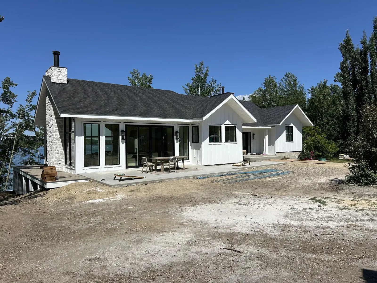 White modern home near Sylvan Lake with crisp siding, a stone chimney and a covered lakeside patio, finished by PJM Home Advantage